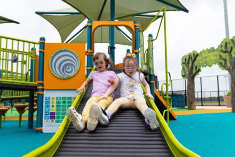 two friends slide side by side down a rollerslide at the recently completed Ed Thompson Inclusive Park playground